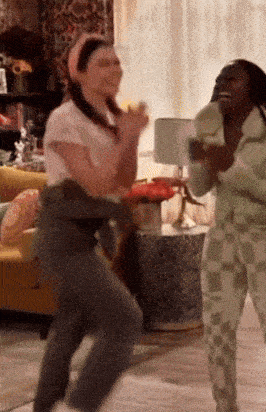 two women are dancing in a living room in front of a couch .