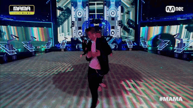 a man in a suit is dancing on a stage with a mnet logo above him
