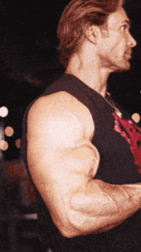 a man with very large muscles is wearing a black tank top with a red skull on it