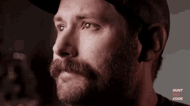 a man with a beard and mustache is wearing a hat and looking to the side .