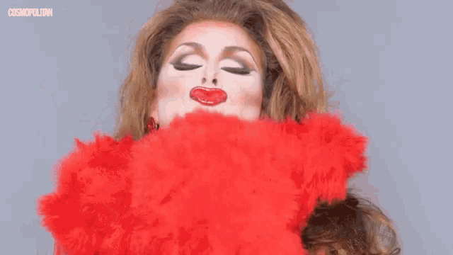 a drag queen is wearing a red boa and making a funny face with her mouth open .