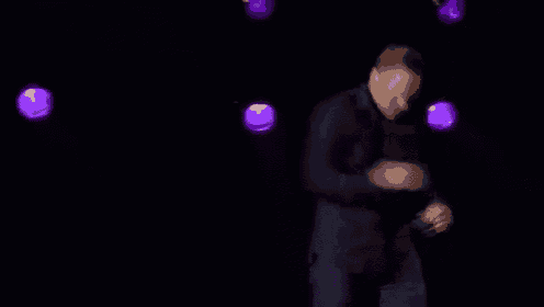 a man in a suit is singing into a microphone on a stage in a dark room .