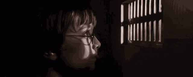a young boy wearing glasses looks out a window with bars