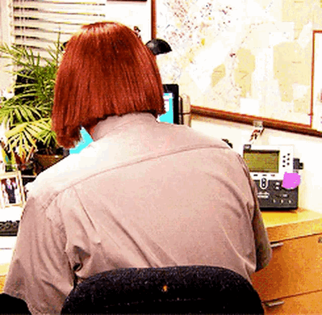 a woman with red hair is sitting at a desk with a telephone and a map on the wall behind her