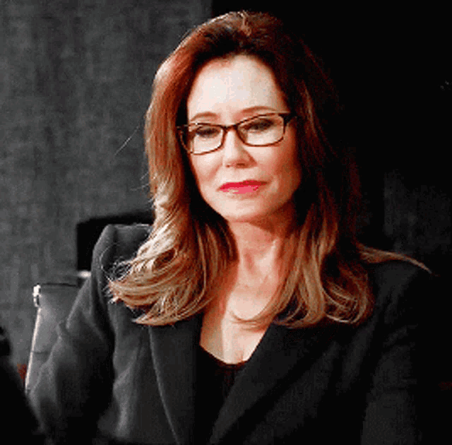 a woman wearing glasses and a black jacket is looking at the camera