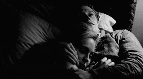 a black and white photo of a man and a woman laying in bed .