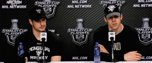 two penguins hockey players are sitting at a table in front of a stanley cup playoffs sign