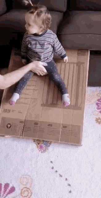a little girl is sitting on a cardboard box with a warning label on it