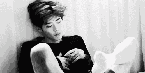 a black and white photo of a man laying on a bed with his legs crossed .