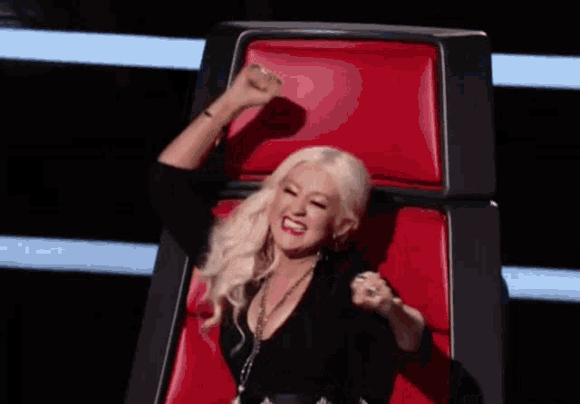 a blonde woman is sitting in a red chair with her arms in the air