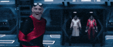 a bald man in a red and black suit stands in front of a shadow character