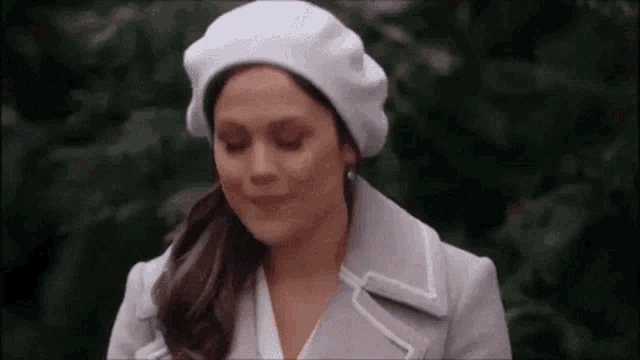a woman wearing a white beret and a white coat is smiling and looking down .