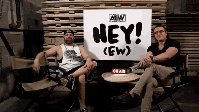 two men are sitting in front of a sign that says hey ( ew )