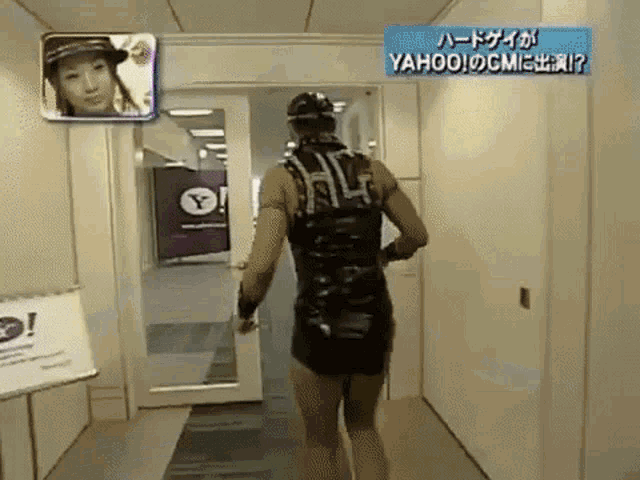 a man in a black outfit is walking down a hallway in front of a sign that says yahoo