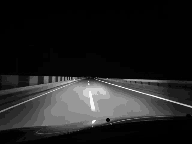 a black and white photo of a highway at night with the headlights on