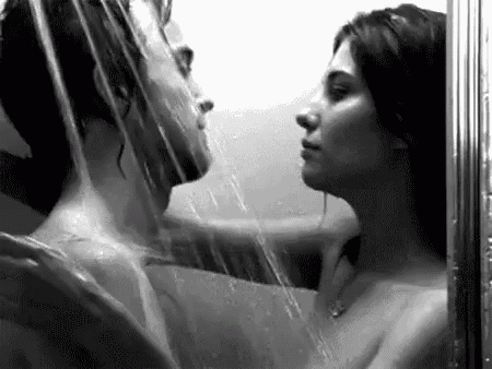 a black and white photo of a man and a woman kissing under a shower .