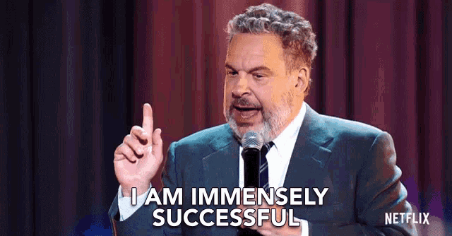 a man in a suit and tie is speaking into a microphone and saying i am immensely successful