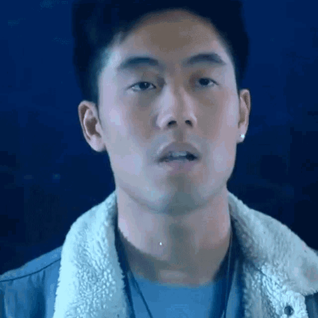 a close up of a man 's face with a blue shirt and a white jacket