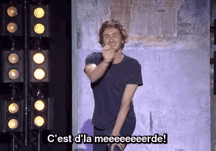 a man in a black shirt is dancing on a stage with the words c'est d' la meeeeeerde behind him