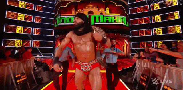 a wrestler is walking down a red carpet in front of a sign that says maha