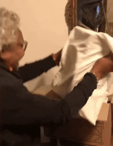 an elderly woman is holding a piece of white cloth in front of a cardboard box that says " fragile " on it
