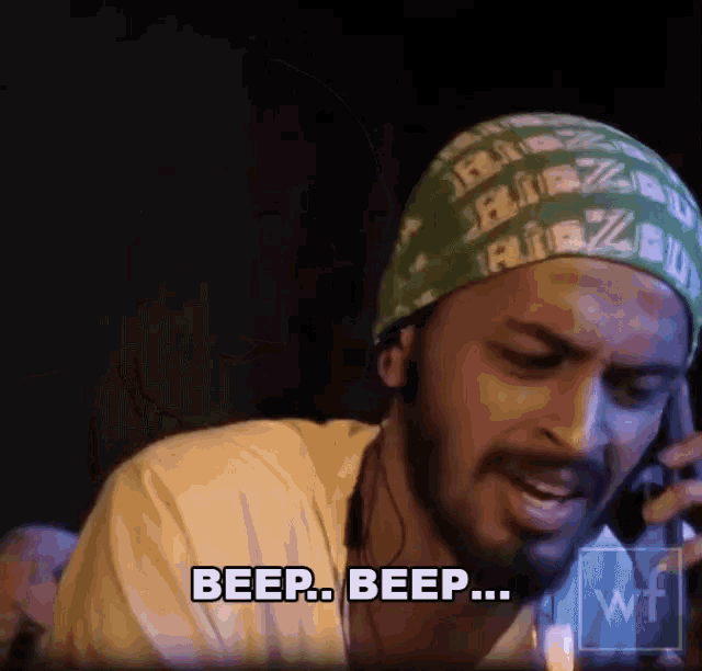 a man wearing a green bandana is talking on a cell phone and saying beep beep