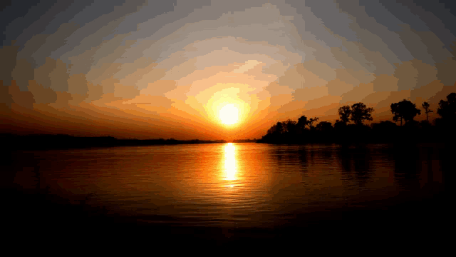 a sunset over a body of water with trees in the background