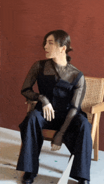 a woman is sitting in a chair wearing a black jumpsuit