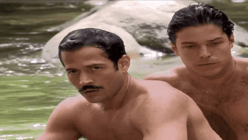 a shirtless man with a mustache is sitting next to another shirtless man