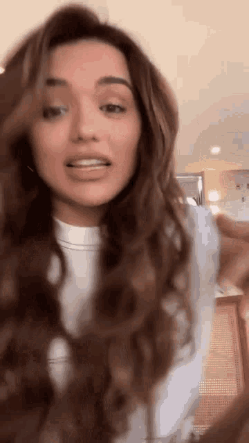 a woman with long brown hair is wearing a white shirt and holding her hair .