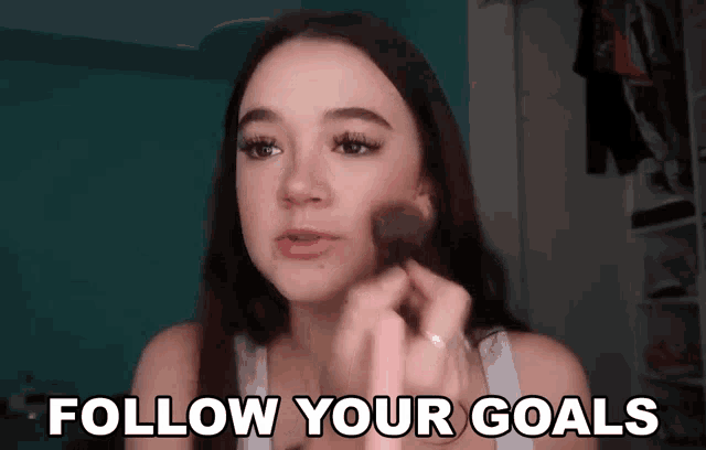 a woman is applying makeup and the words follow your goals are above her