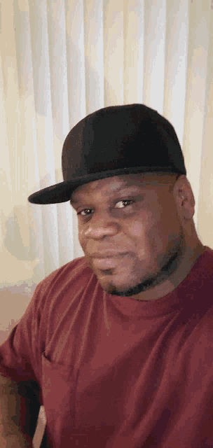 a man wearing a black hat and a maroon shirt looks at the camera