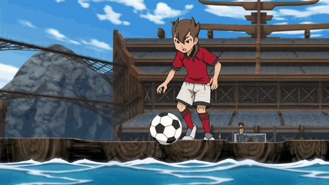 a boy in a red shirt is kicking a soccer ball over a wooden dock