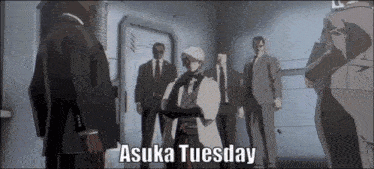 a group of men in suits and ties are standing in a room with the words asuka tuesday above them .