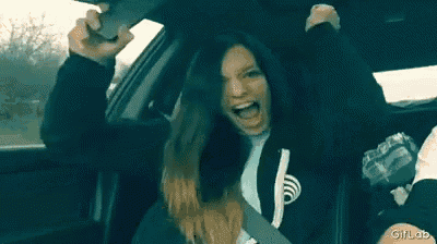 a woman is sitting in the back seat of a car with her arms in the air and her mouth open .