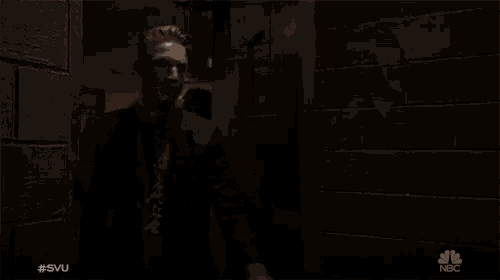 two men in suits and ties are walking in a dark hallway with a nbc logo in the corner