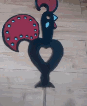 a black rooster with a red tail and a blue beak is on a stick