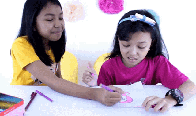 two young girls are sitting at a table drawing with markers