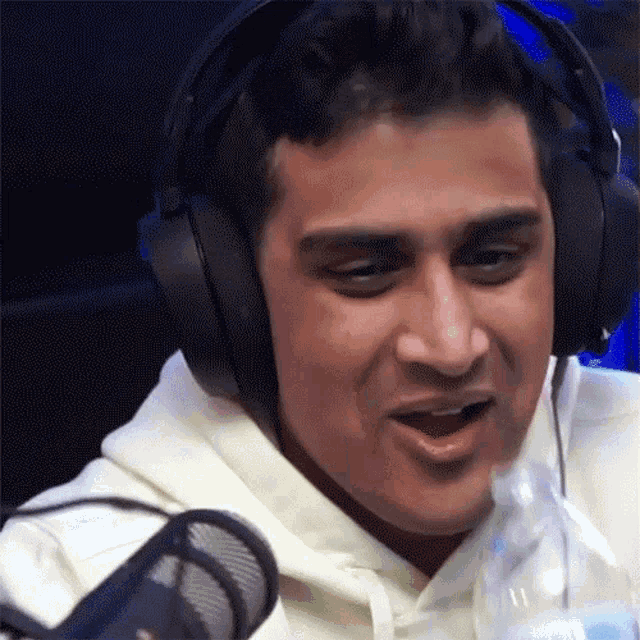 a man wearing headphones is sitting in front of a microphone with his mouth open .