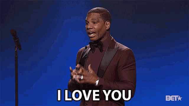 a man in a suit stands in front of a microphone and says i love you in front of a bet logo