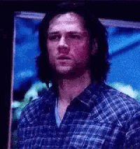 a man in a blue plaid shirt is standing in front of a blue wall .