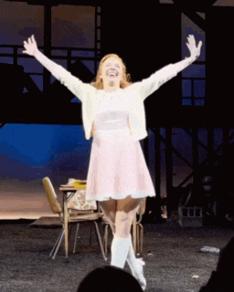 a woman in a pink dress stands on a stage with her arms in the air