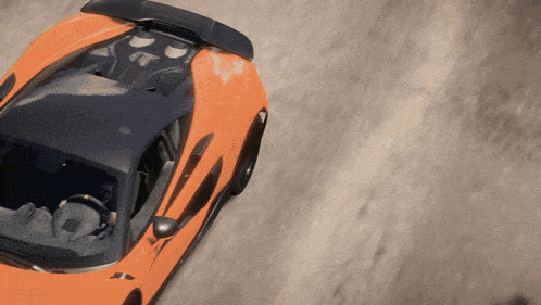 an orange sports car with a black wing is driving down a dirt road