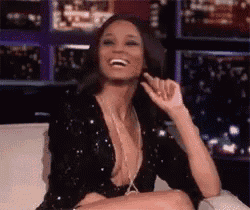 a woman in a black sequined top is sitting on a couch and smiling .