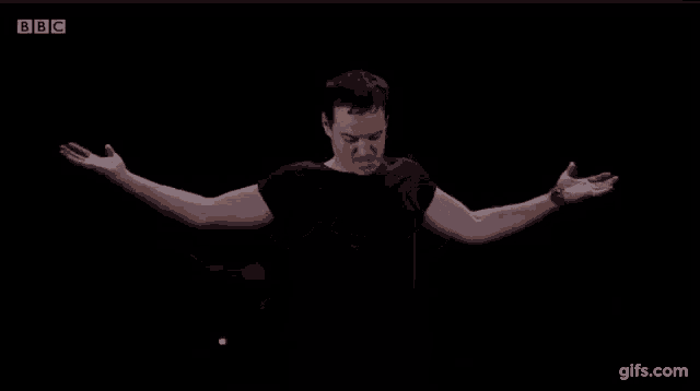 a man in a black shirt is making a funny face while standing in front of a black background .