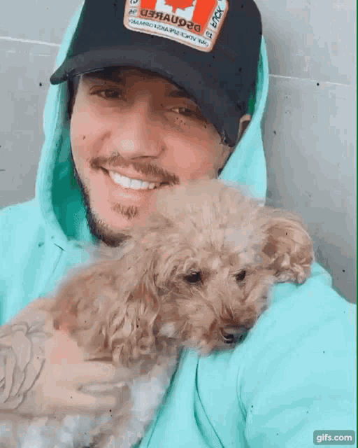 a man wearing a green hoodie and a black hat holds a dog