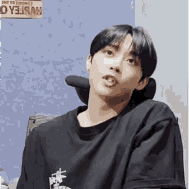 a young man wearing a black shirt is sitting in front of a blue wall with a sign that says white tea