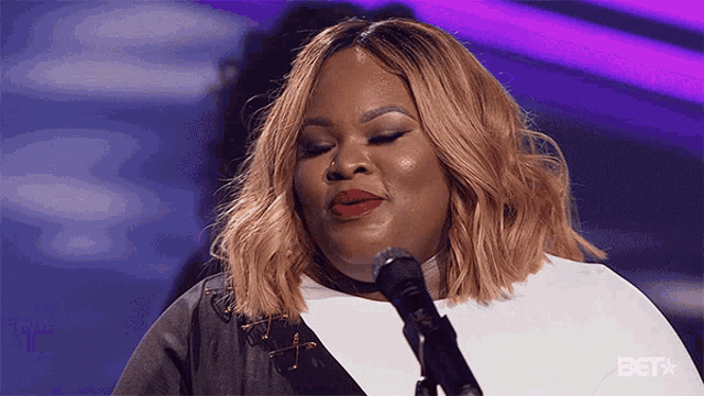 a woman singing into a microphone with a bet logo in the corner