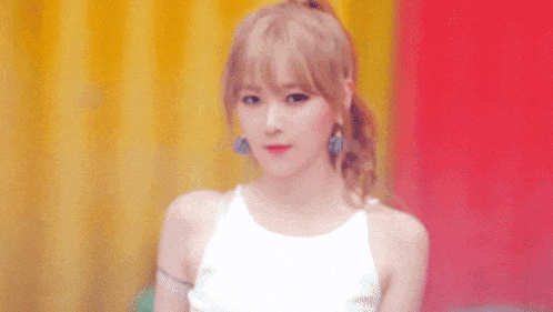 a woman wearing a white tank top and blue earrings is looking at the camera .