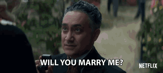 a man in a suit is holding a ring and asking if he will marry him